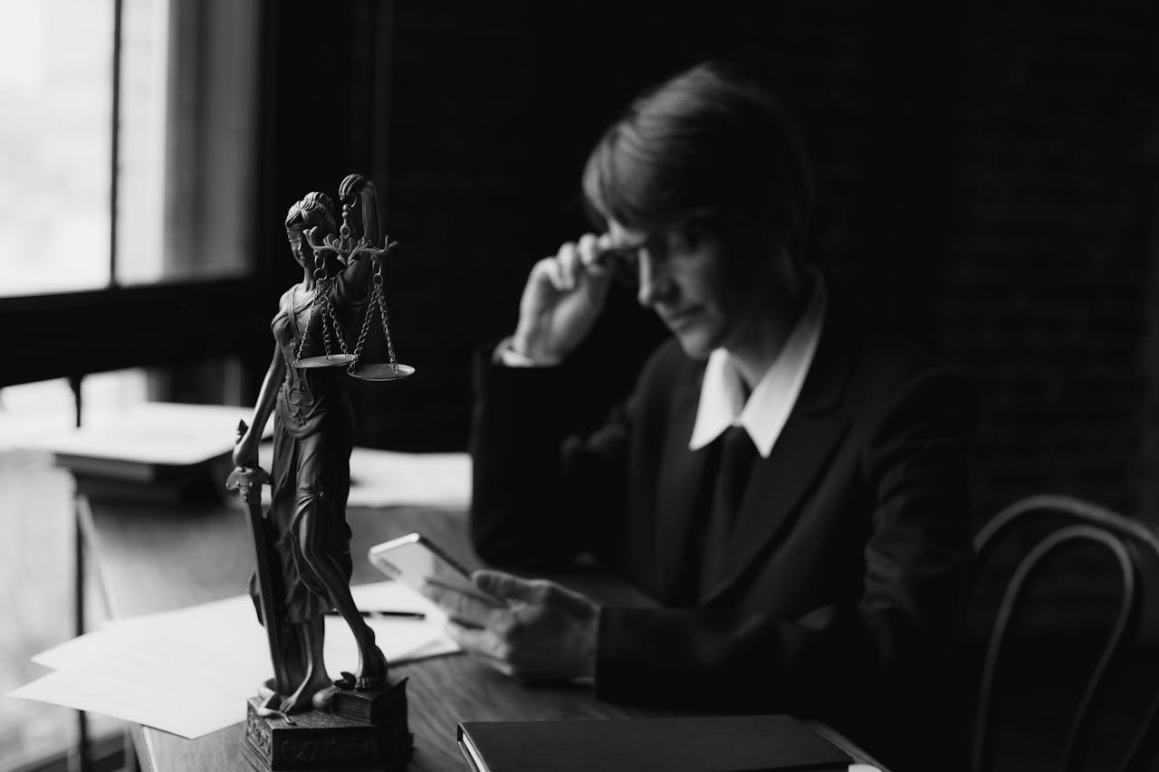 About Black-and-white image of an attorney in an office with Lady Justice statue and smartphone, symbolizing modern legal concepts.